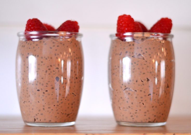 two glass cups on table with chocolate chia pudding and raspberries on top