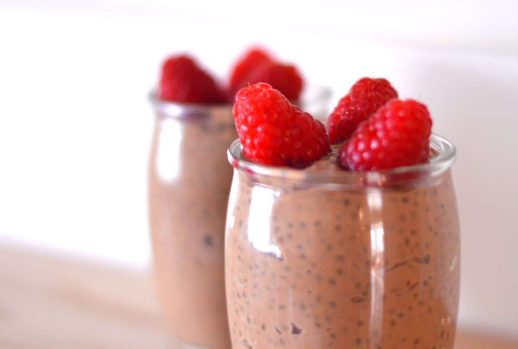 Two small glass cups side by side filled with chocolate chia pudding and topped with raspberries