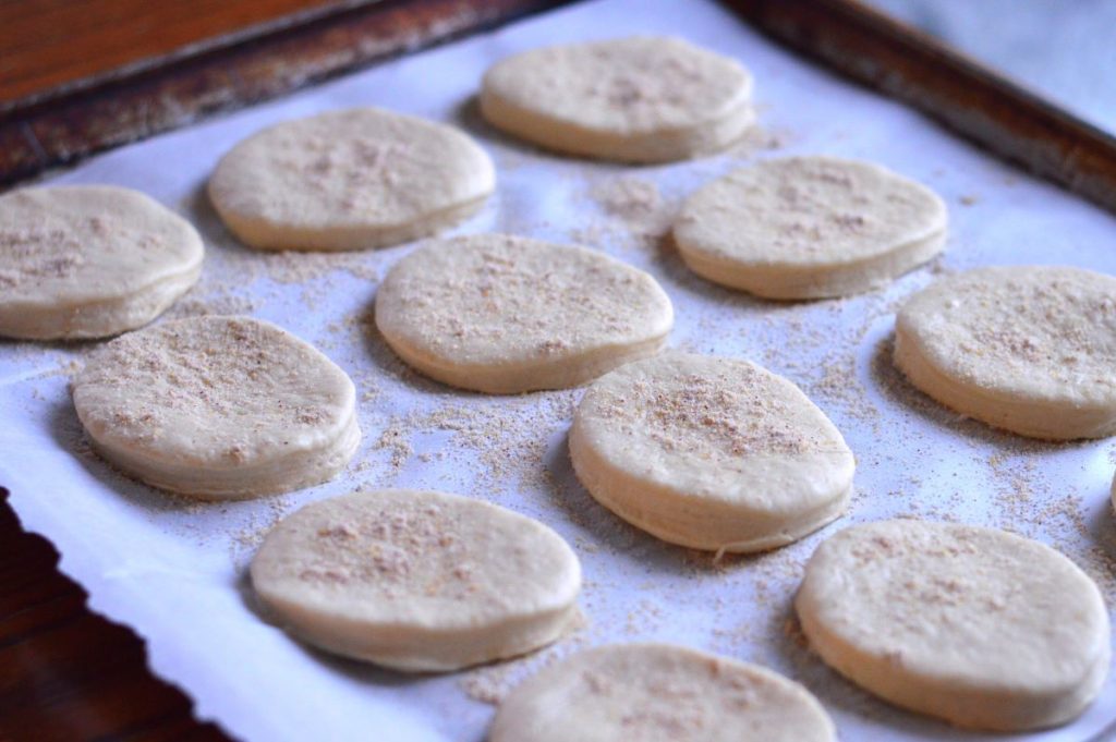 tray of uncooked sourdough english muffins on tray lined with parchement paper and sprinkled with cornmeal
