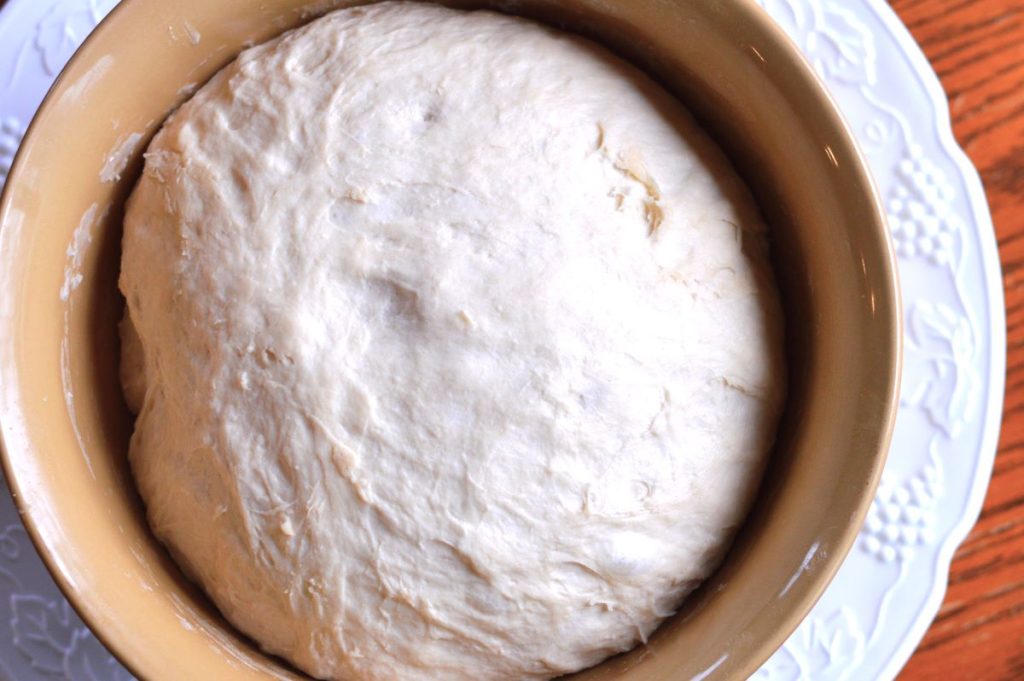 risen sourdough English muffin dough in ceramic bowl