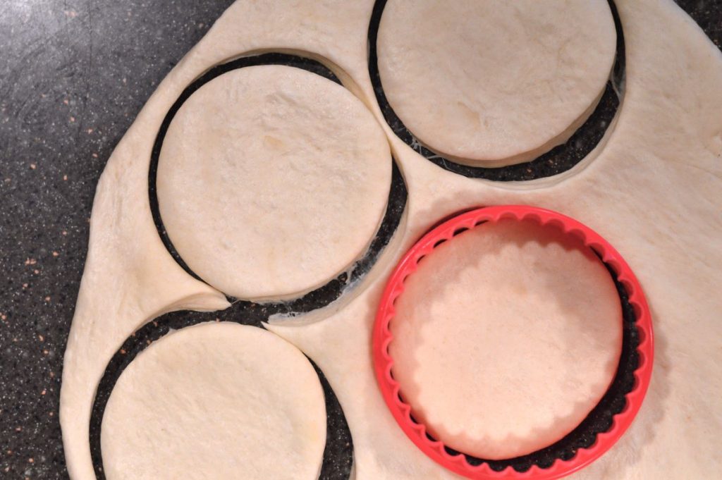rolled out english muffin dough being cut out with 3 inch round cookie cutter