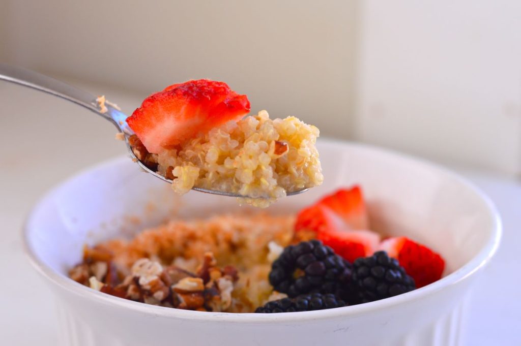 one spoonful of quinoa with strawberries above bowl of quinoa, berries, and pecans