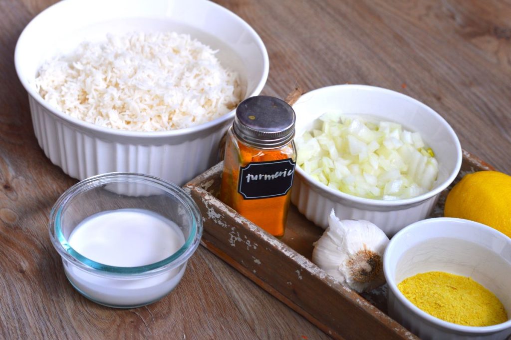 bowl of white rice, bowl of onions, lemon, garlic, bowl of nutritional yeast, bowl of coconut milk, bottle of turmeric spic