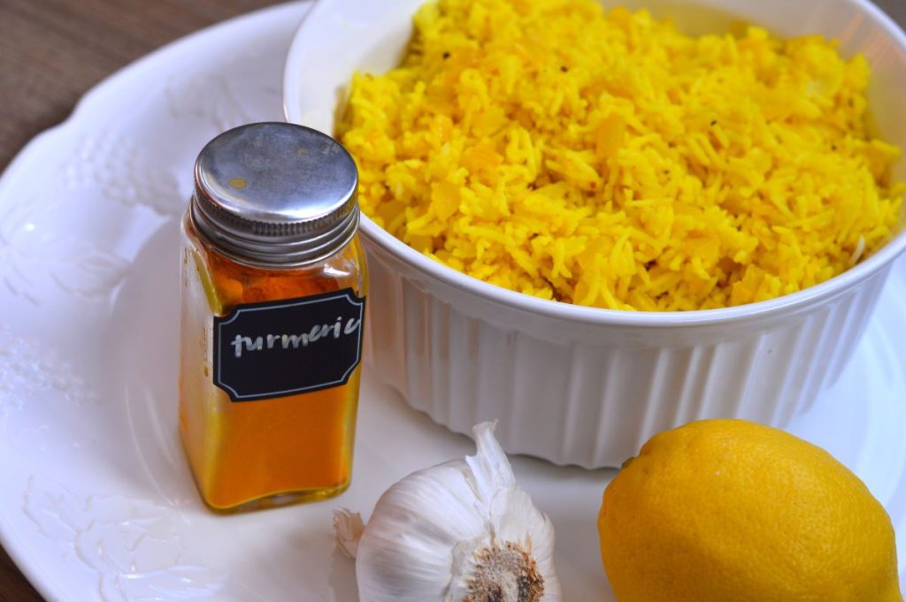 bottle of turmeric spic next to bowl of yellow rice