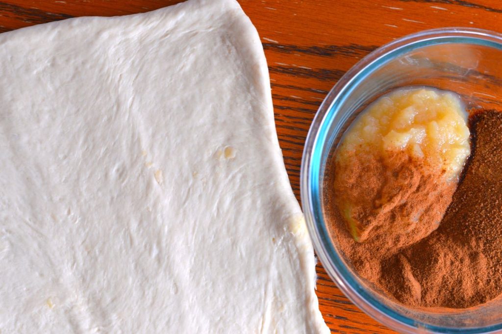 rolled dough next to bowl of applesauce, coconut sugar, and cinnamon