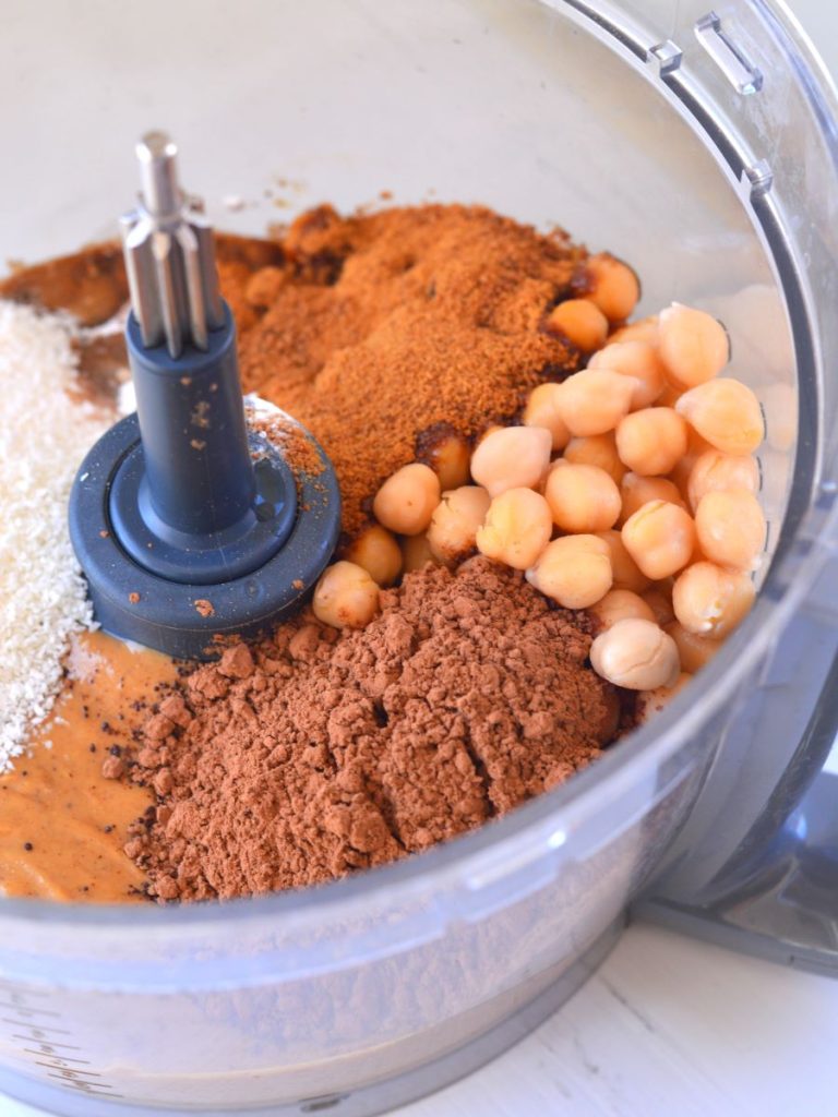 chickpeas, cacao, coconut sugar, cinnamon, coconut, and other ingredients for cookies in food processor bowl.