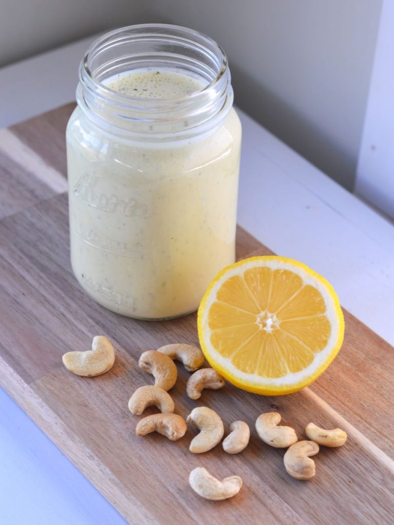 jar of vegan ranch dressing next to raw cashews and half lemon