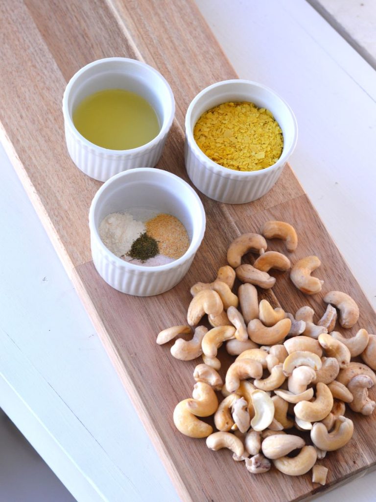 bowls of lemon juice, nutritional yeast, and spices next to soaked raw cashews
